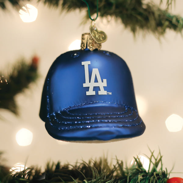 Los Angeles Dodgers cap ornament hanging on a lit Christmas tree with warm bokeh lights and pine branches