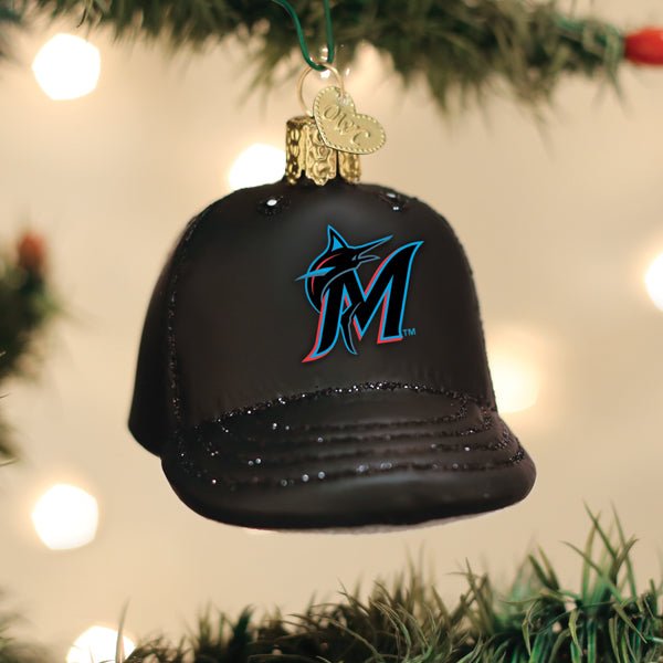 Miami Marlins cap ornament hanging on a lit Christmas tree with warm bokeh lights and pine branches