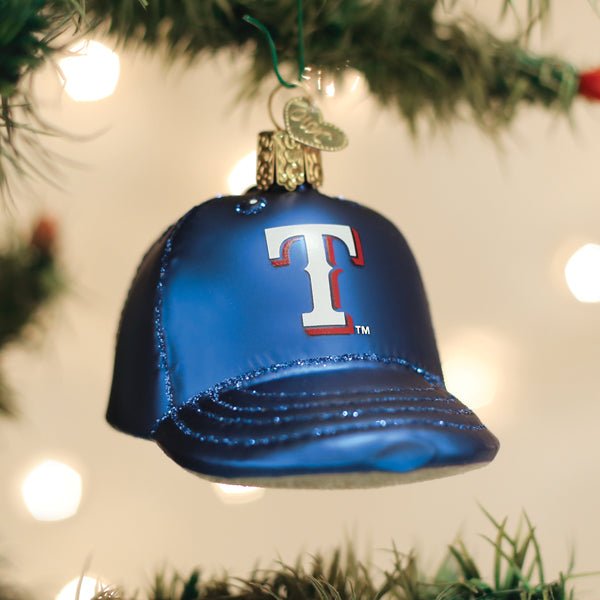 Texas Rangers cap ornament hanging on a lit Christmas tree with warm bokeh lights and pine branches