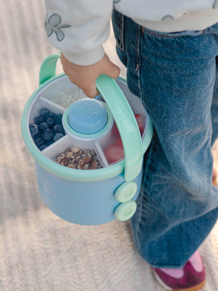 Child carrying the blue Lunch Stack by its handle, snack spinner filled with fruit