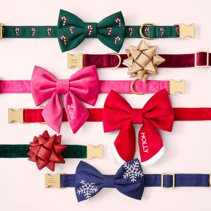 Six holiday bow collars on pink, including candy canes, gold and red gift bows, pink and red sailor bows, and snowflakes.