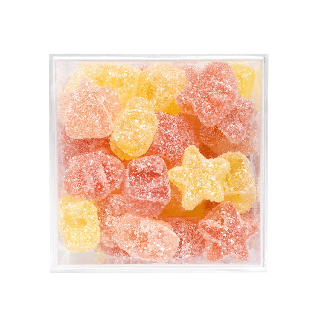 A clear square plastic container filled with sugar-coated gummy candies in yellow and pink-orange tones, photographed on a plain white background.