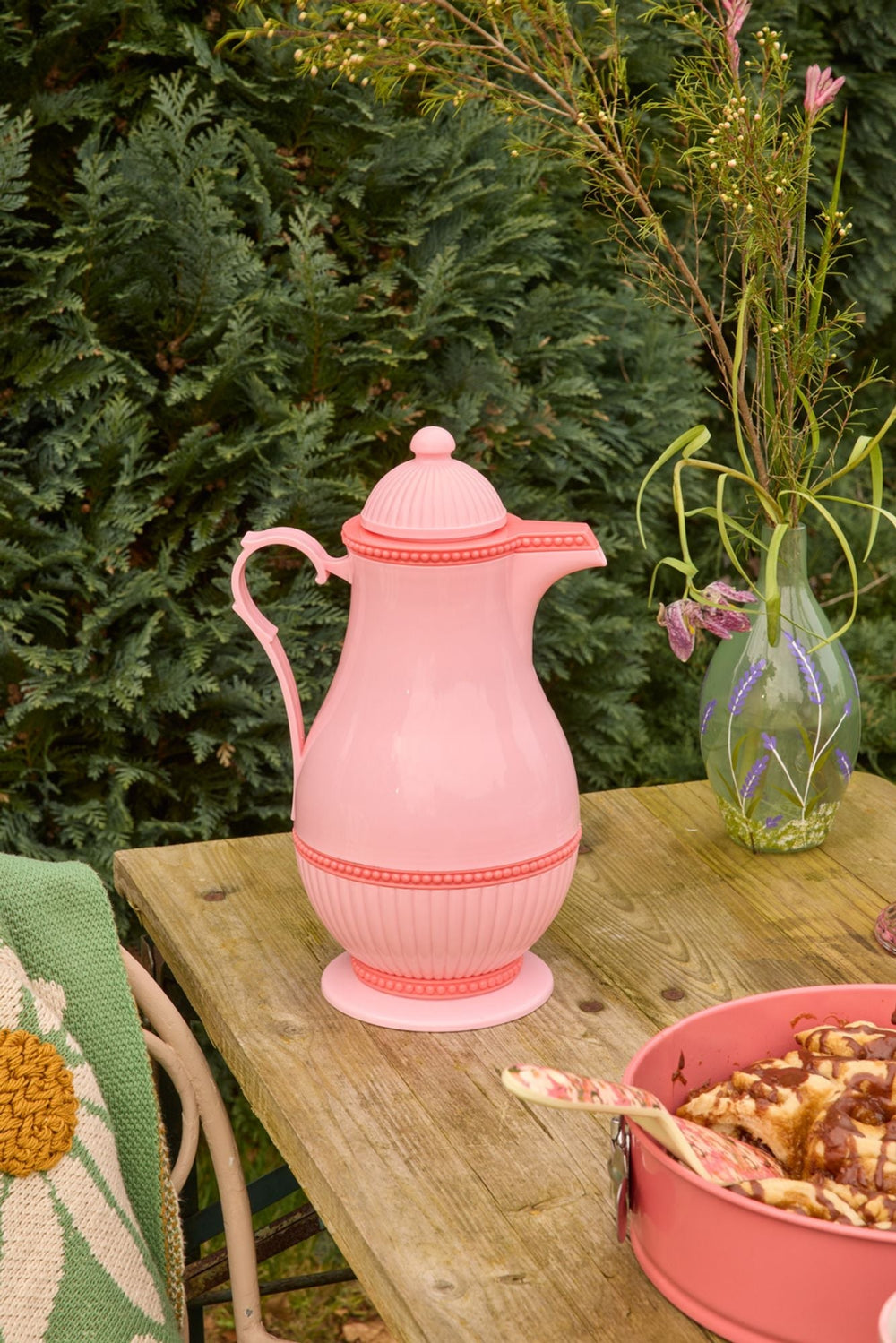Pink Thermo jug on a wooden garden table with a glass vase of wildflowers and a pink bowl of pastries
