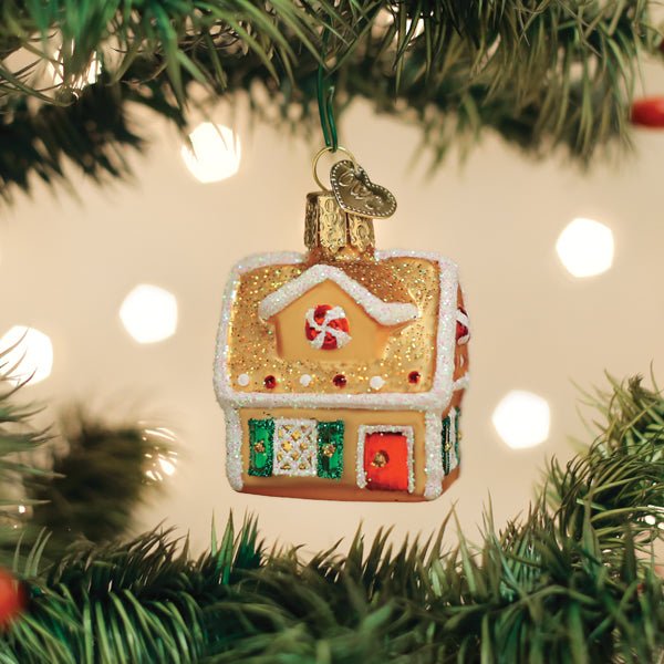 Gingerbread house ornament hanging on a lit Christmas tree with warm glowing lights behind