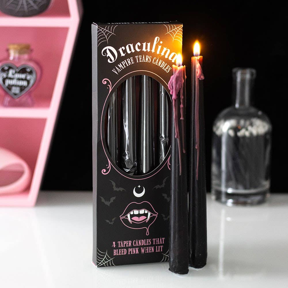 Two lit black tapers bleeding pink wax beside the Draculina box in a pink and black Halloween vignette