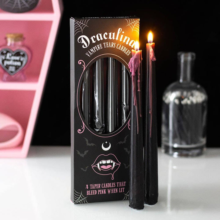 Two lit black tapers bleeding pink wax beside the Draculina box in a pink and black Halloween vignette