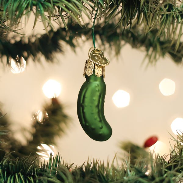 Mini Christmas pickle ornament hidden on a branch of a lit Christmas tree