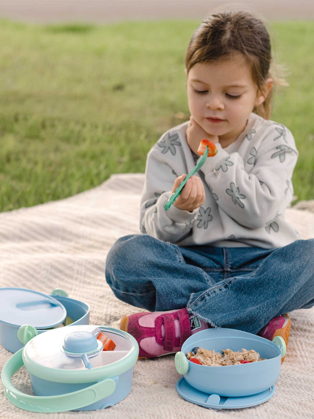 Toddler on a picnic blanket with the blue Lunch Stack compartments opened out