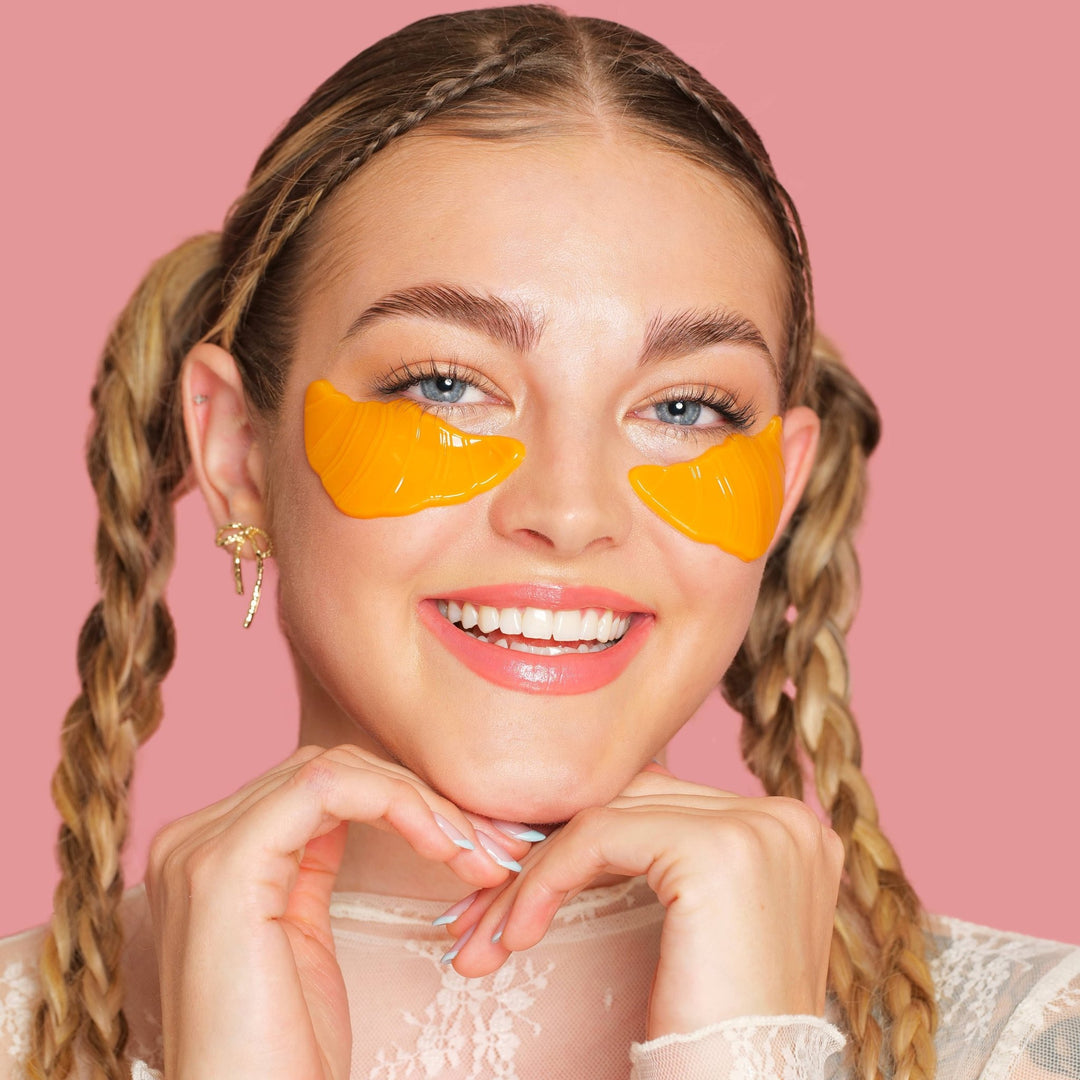 Model with braided pigtails smiling in golden croissant under eye patches, a treat for a brunch or spa party