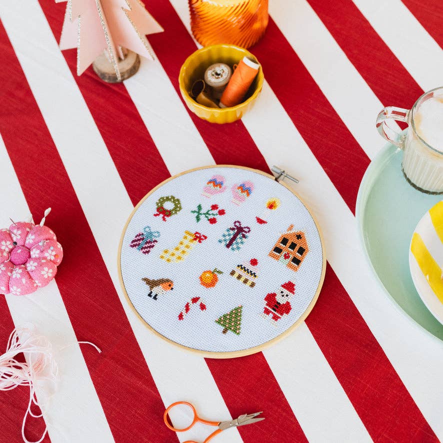 Finished Christmas cross stitch sampler on candy striped tablecloth with pincushion