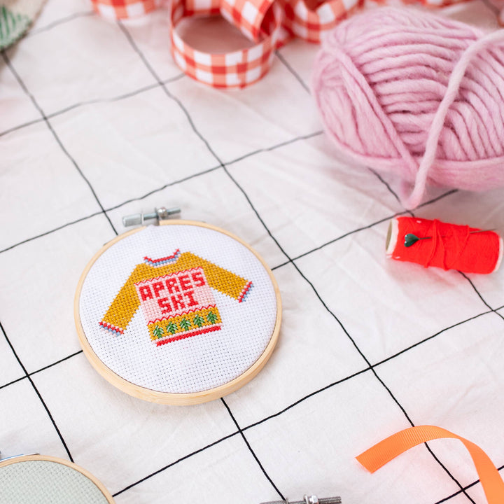 Apres ski sweater cross stitch hoop on grid cloth with pink yarn and gingham ribbon