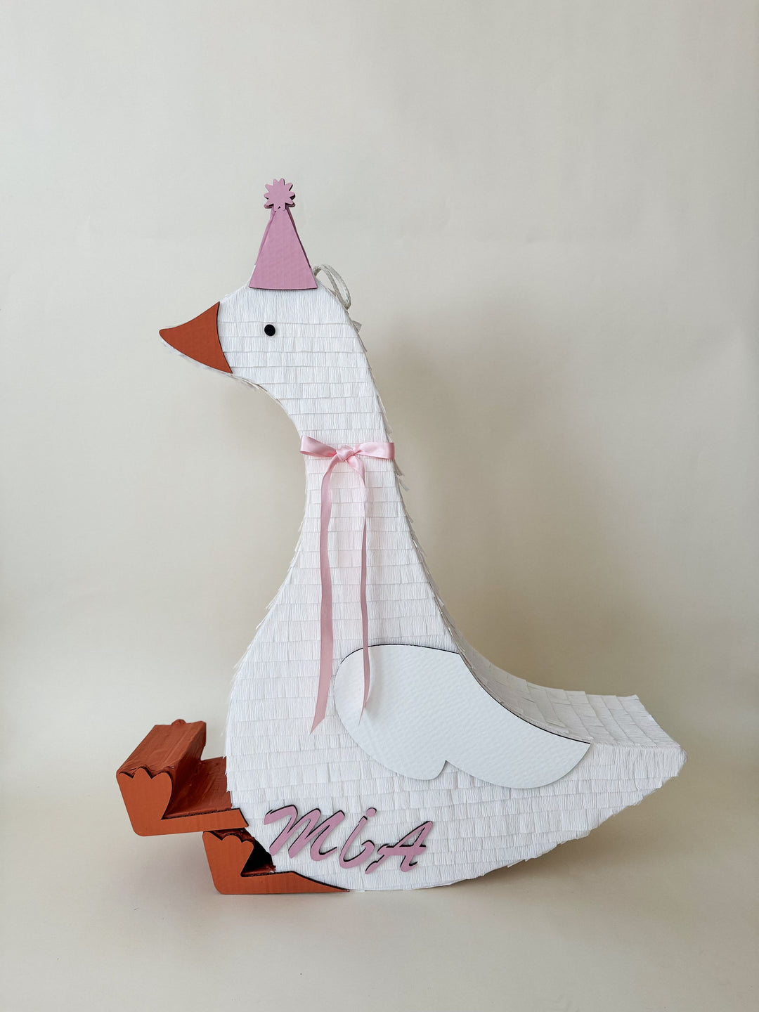 Tall white sitting goose piñata with a pink party hat and pink ribbon bow, shown with a personalized name, for a farm party