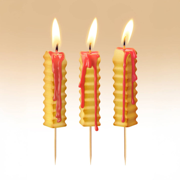 Three french fry birthday candles lit on warm beige background, red ketchup wax melting down sides during birthday party
