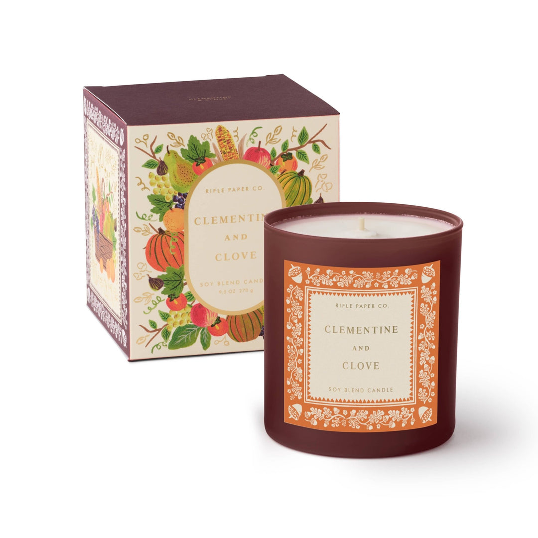 Clementine and Clove candle in dark plum glass with orange acorn label beside its harvest fruit gift box
