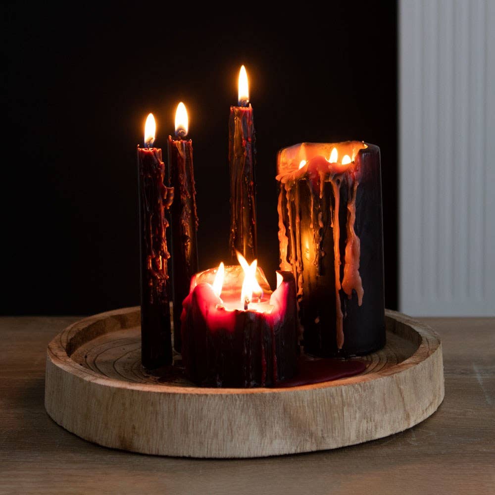 Lit black taper and pillar candles dripping red and cream wax on a wooden tray for a moody Halloween party