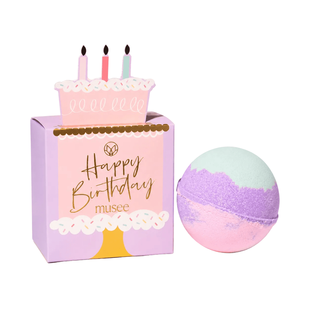 Mint, purple, and pink bath bomb beside lavender Happy Birthday cake box, a kids birthday party favor