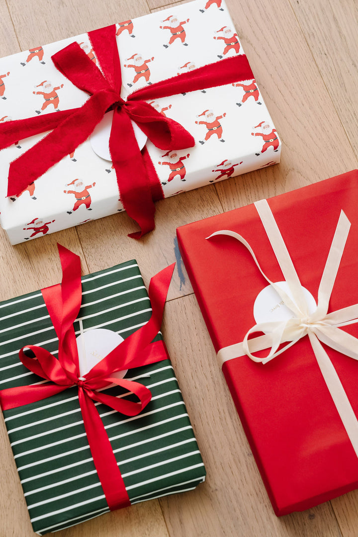 Angled view of Santa print, green stripe, and solid red gifts with velvet and satin bows on wood