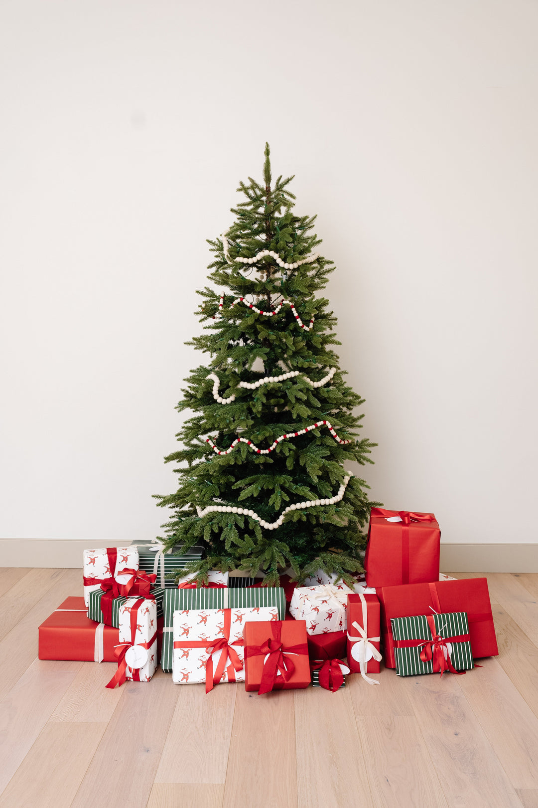 Christmas tree with Santa print, green stripe, and red gifts arranged on a pale wood floor