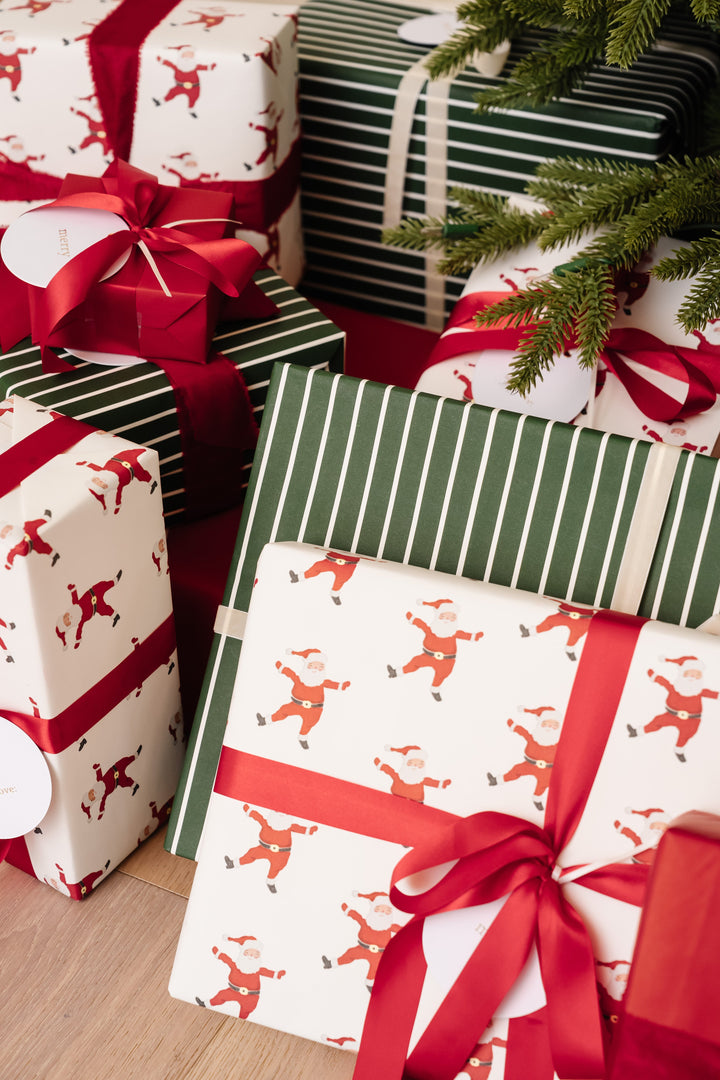 Santa print gifts with red satin ribbon stacked under Christmas tree branches
