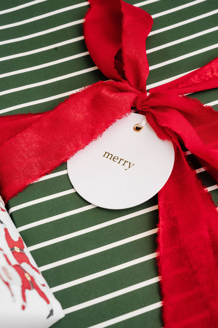 Round gold foil merry tag with frayed red velvet on green and white striped wrapping