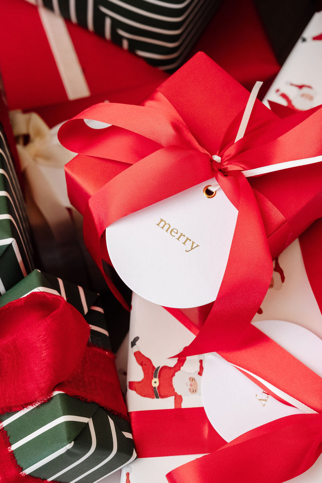 Round merry gift tag hanging from a red satin bow on a solid red Christmas present