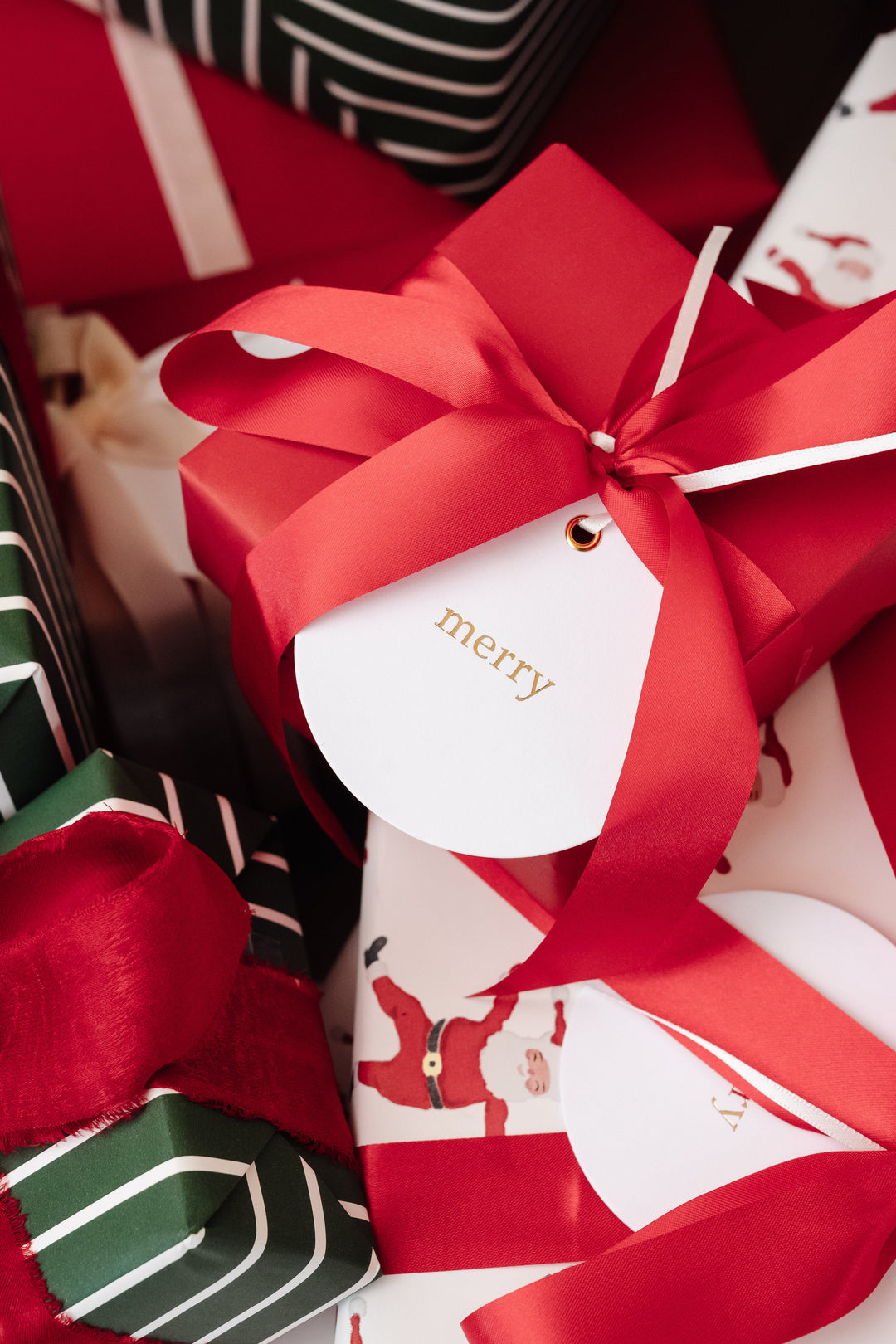 Solid red gift with a red satin bow and round letterpress merry tag in gold foil