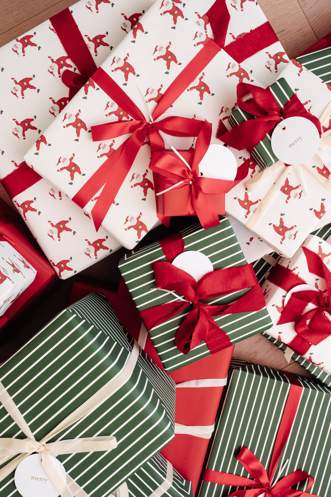Top-down heap of Santa print and green striped Christmas gifts with frayed red velvet bows