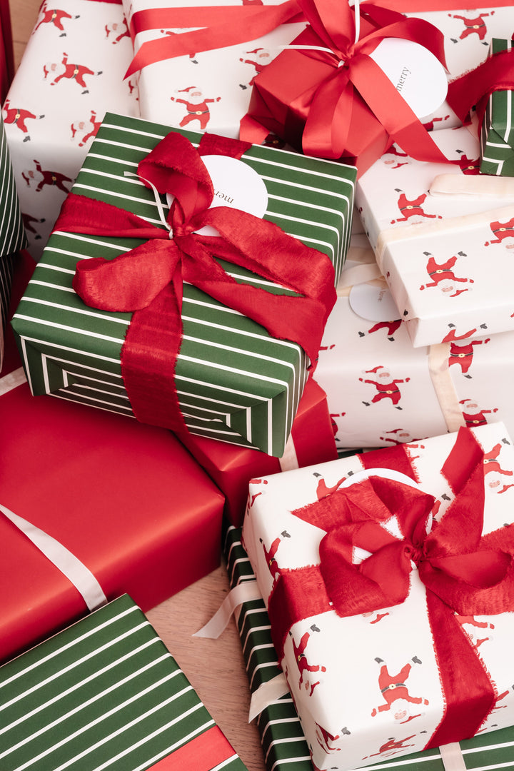 Close pile of Santa print, red, and green striped Christmas presents with red ribbon