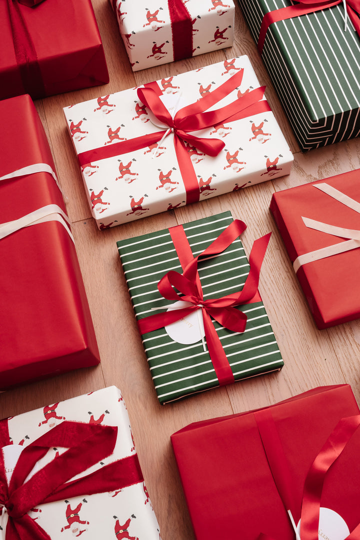 Overhead view of Santa print, solid red, and green stripe gifts with red bows on a wood floor