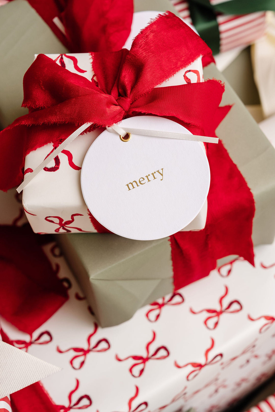 Round merry tag in gold foil on bow print gift wrap tied with frayed red velvet ribbon