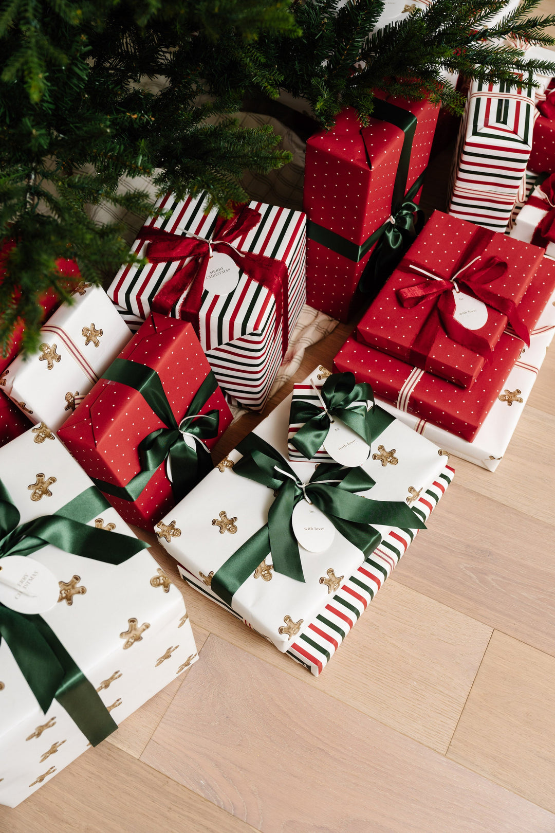 Gingerbread and red striped Christmas presents stacked under the tree on a pale wood floor