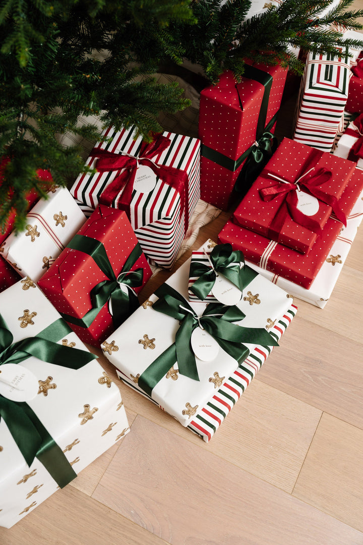 Gingerbread and red striped Christmas presents stacked under the tree on a pale wood floor