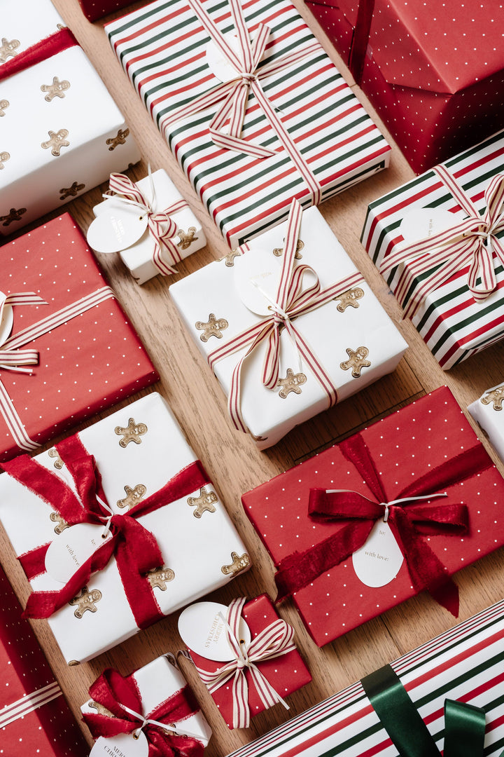 Overhead rows of gingerbread and red polka dot wrapped gifts on a wood floor with oval gift tags