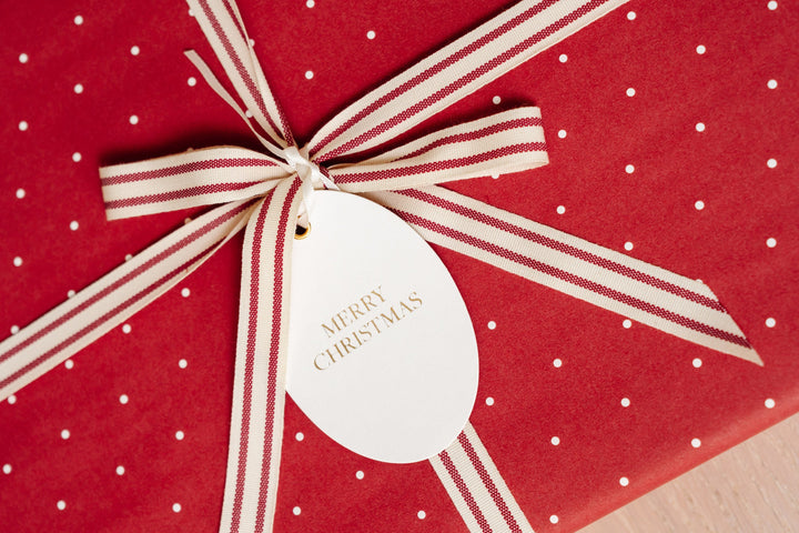 Red polka dot gift wrap tied with red and cream striped ribbon and a gold foil Merry Christmas tag