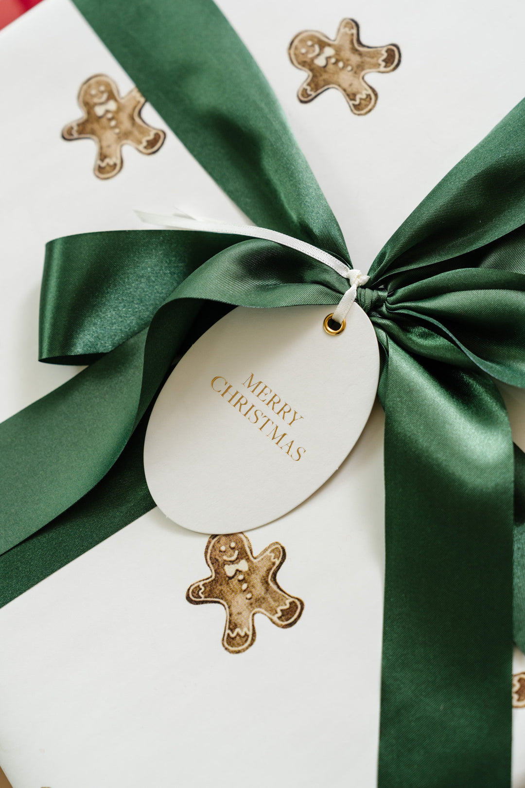 Gingerbread man wrapping paper with a green satin bow and oval Merry Christmas tag in gold foil