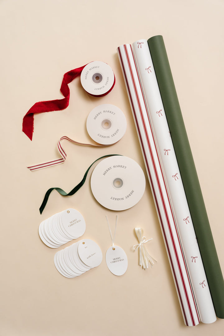 Petite bows Christmas wrapping paper kit flat lay: three rolls, velvet and striped ribbons, and oval gold foil tags