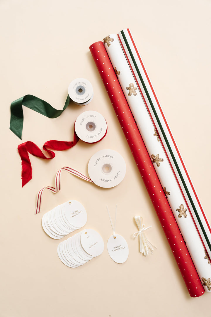 Gingerbread Christmas wrapping paper kit flat lay: rolls, red velvet, green satin, and striped ribbon, and oval tags