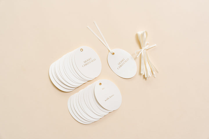 Fanned stack of oval gold foil letterpress gift tags with a bundle of cream tying ribbon