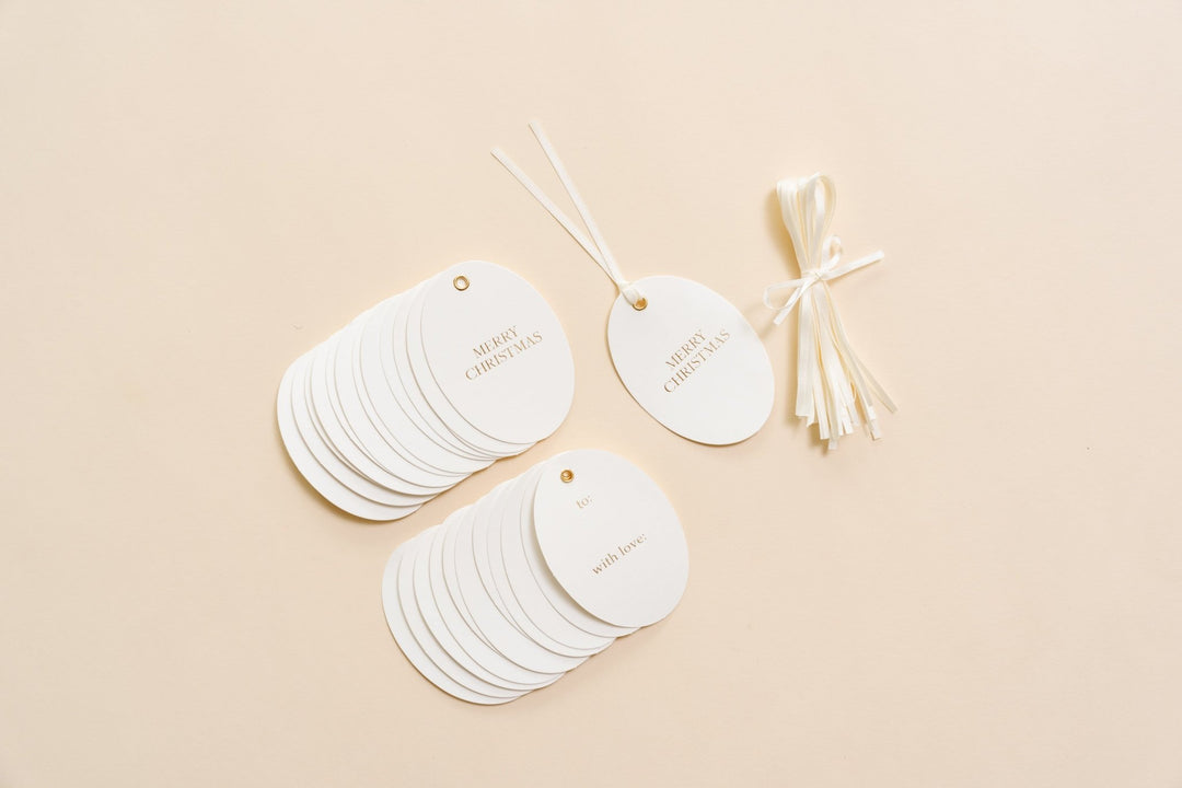Stack of oval letterpress Christmas gift tags in gold foil with a bundle of cream satin ribbon