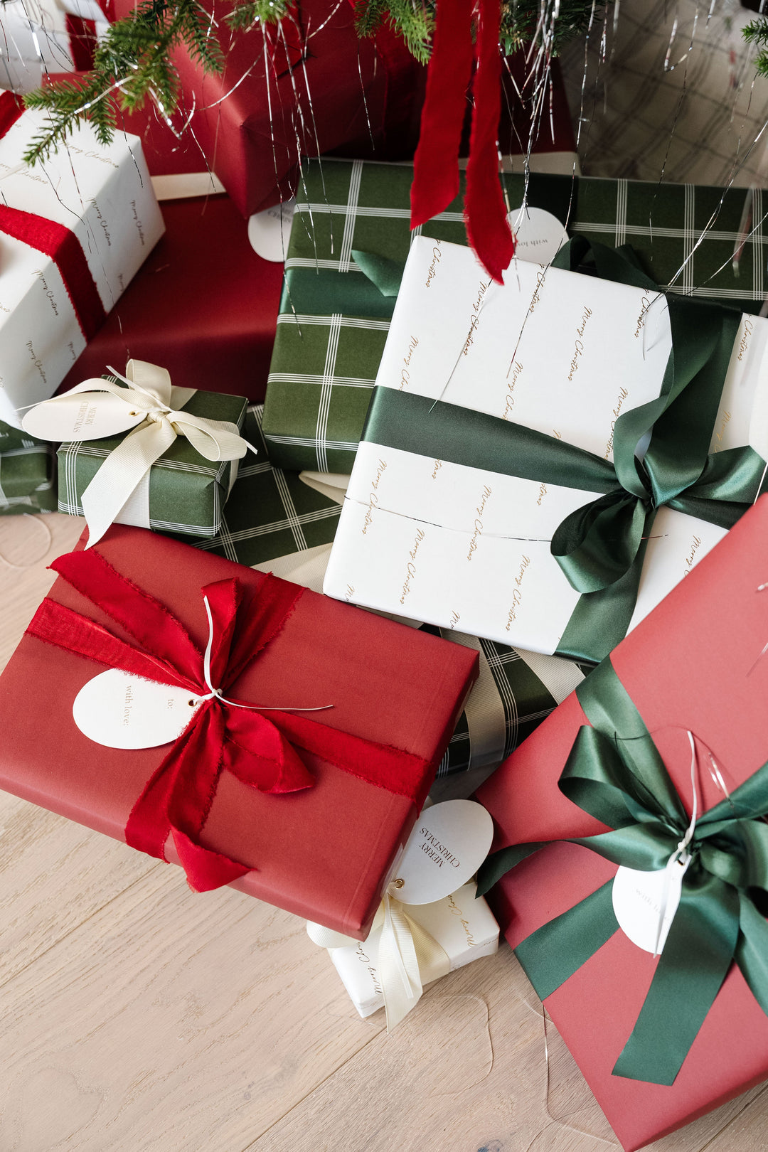 Plaid, red, and gold script presents piled under a Christmas tree on a wood floor