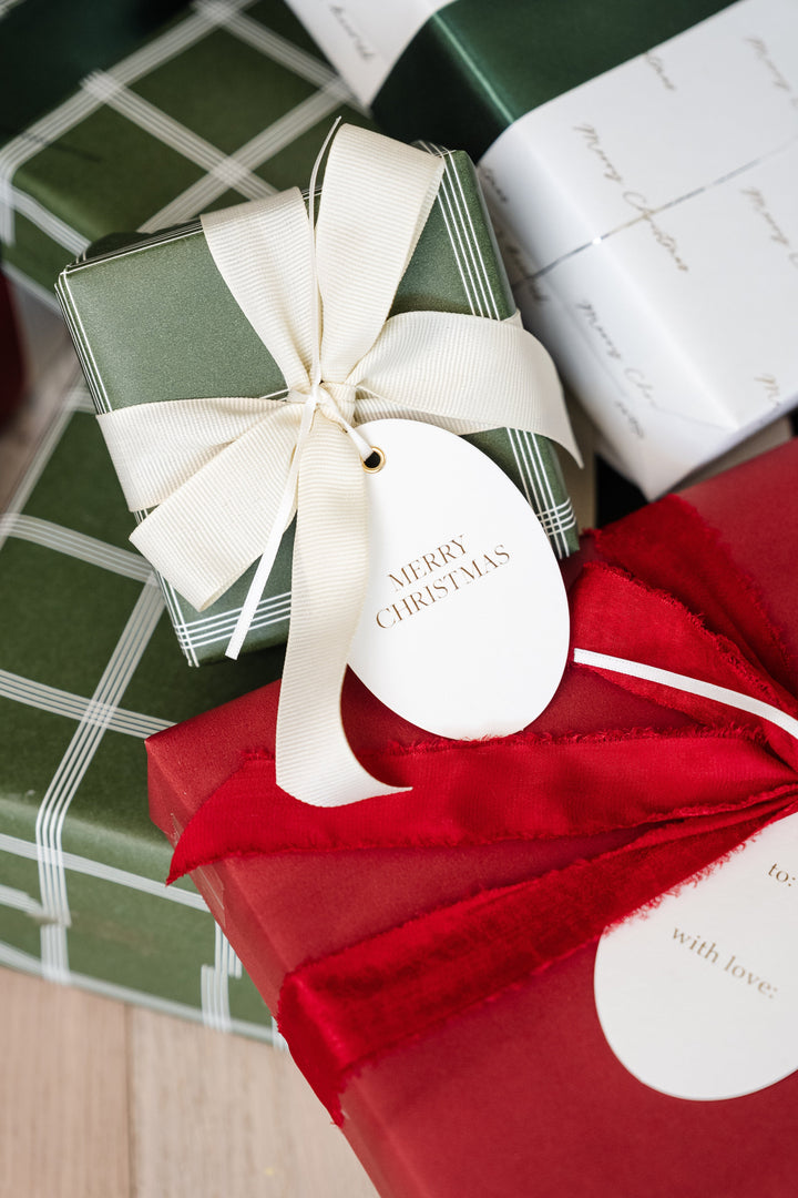 Plaid and red Christmas gifts close up with cream grosgrain bow, red velvet, and oval tags