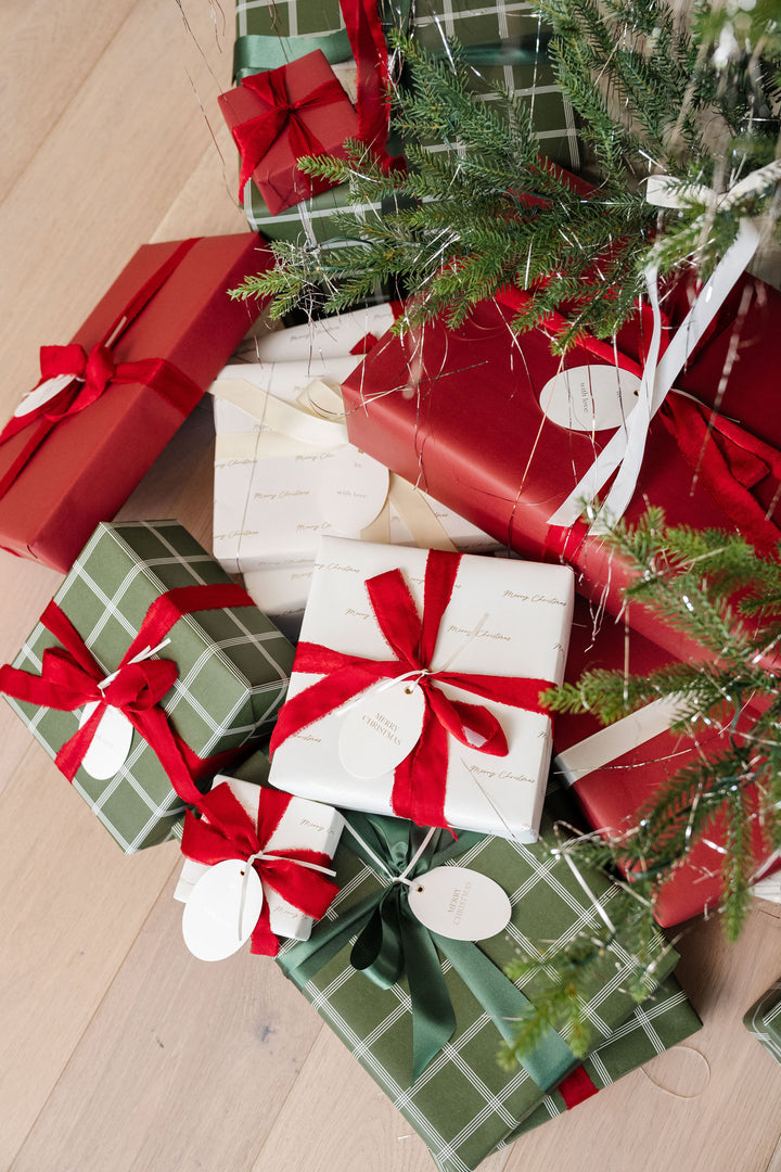 Gifts with red velvet and green satin bows heaped below evergreen branches