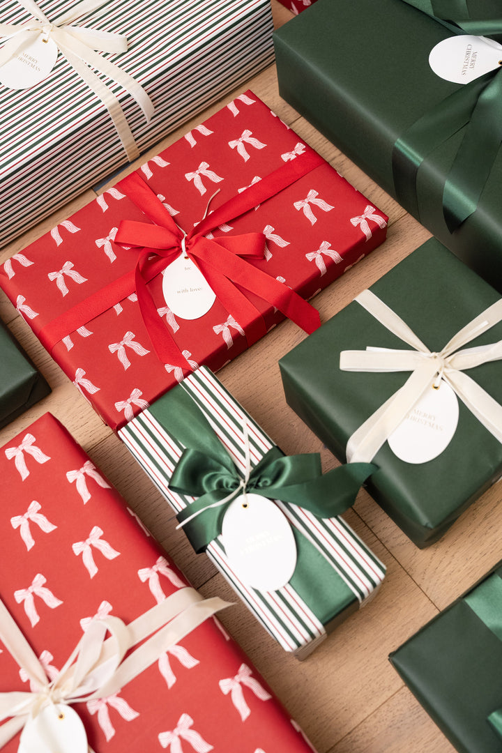Overhead rows of wrapped Christmas gifts in red bow print and green paper with oval Merry Christmas tags