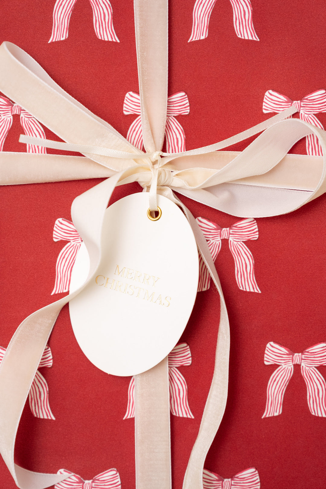 Oval letterpress tag hanging from cream velvet ribbon on red bow print gift wrap