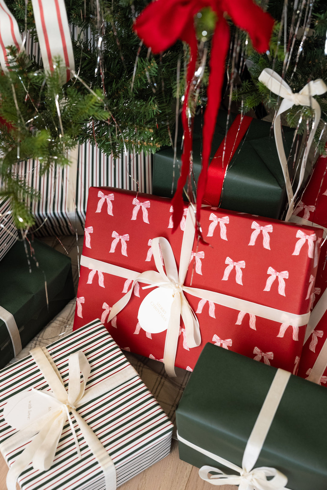 Gifts in red bow wrapping paper with red satin bows stacked beneath Christmas tree branches
