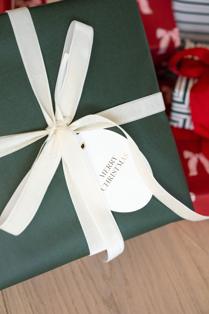 Oval gold foil tag tied with cream velvet ribbon on a forest green wrapped present
