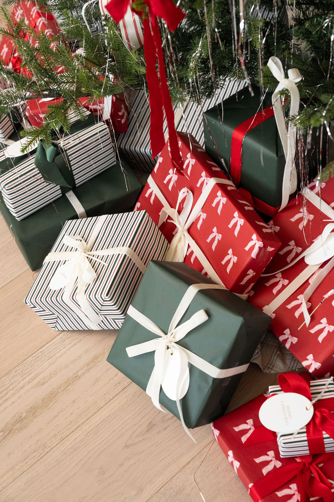 Wrapped gifts in bow, stripe, and green paper piled under a decorated Christmas tree
