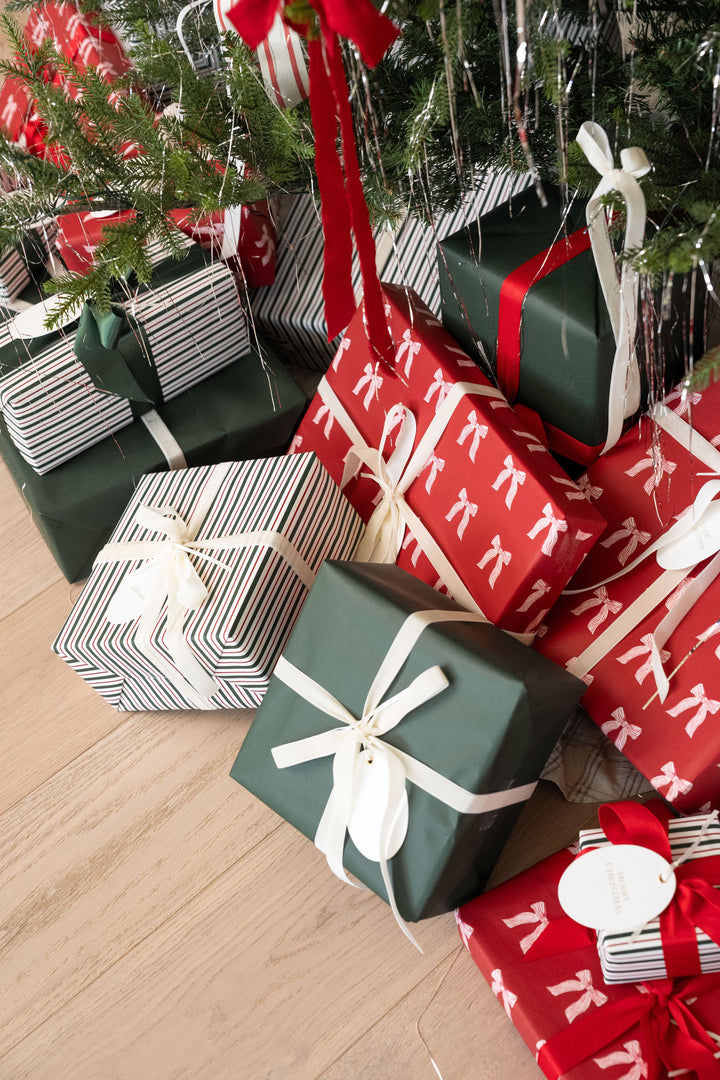 Wrapped gifts in bow, stripe, and green paper piled under a decorated Christmas tree