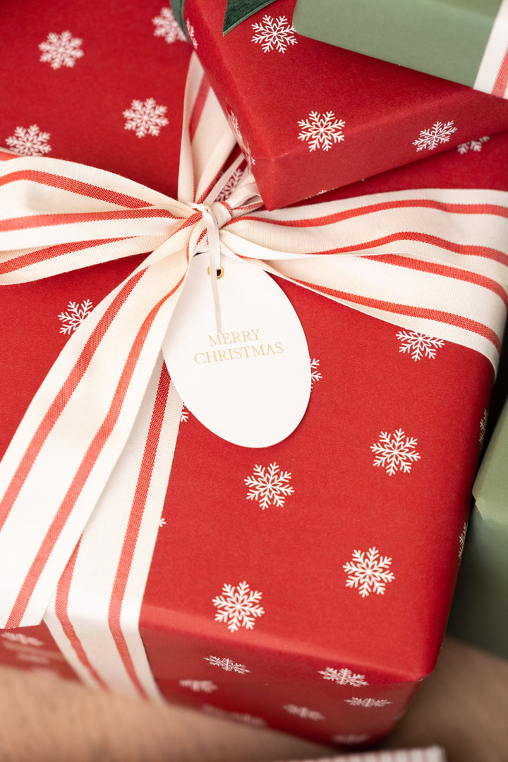 Merry Christmas oval tag on a red snowflake gift with a wide striped cotton bow