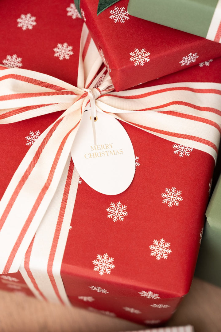 Red snowflake gift wrap with a wide striped cotton bow and gold foil Merry Christmas tag